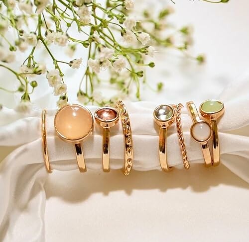 Elegant gold rings with colorful gemstones on a white fabric.