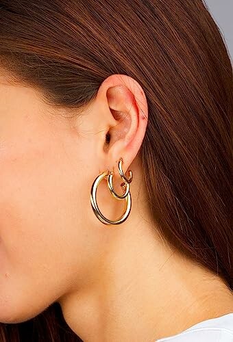 Close-up of a woman's ear wearing gold hoop earrings.