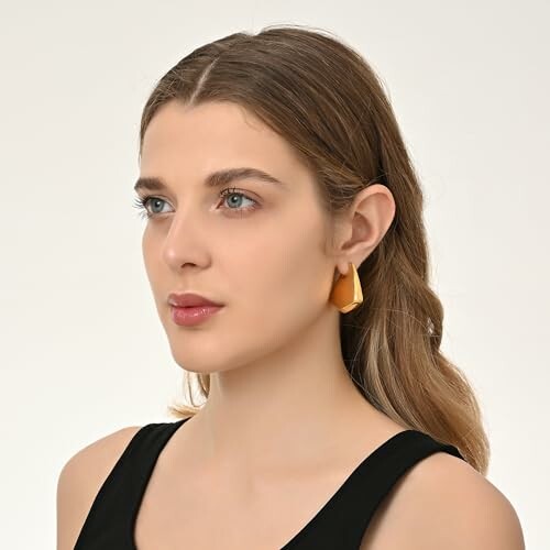 Woman with long brown hair wearing gold earrings and a black top